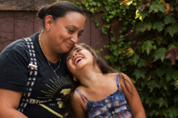 Susanna and daughter laugh together in front of their home.